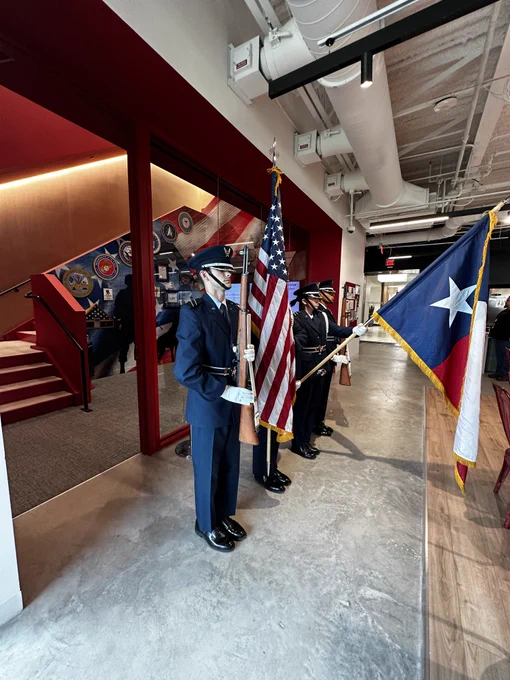 Color Guard procession with U.S. and Texas flags, proceeding inside a building with visible ductwork on the ceiling.