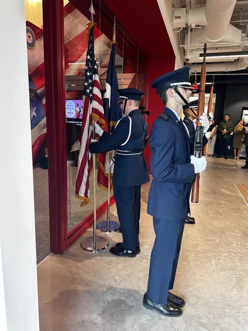 Two U.S. Air Force Honor Guard members standing at attention with a folded American flag in a display case at a memorial service.