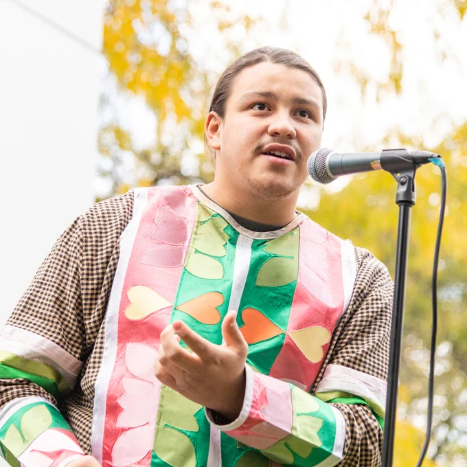 A person in colorful clothing speaks into a microphone outdoors