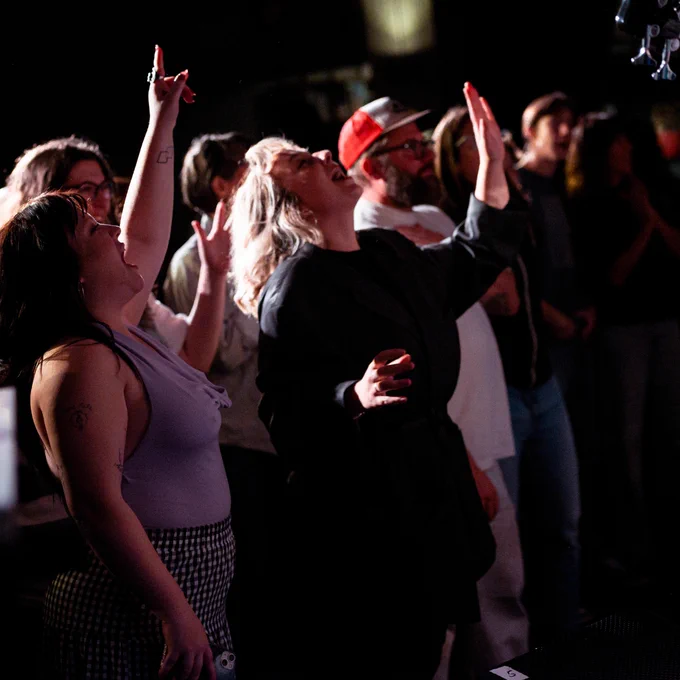A group of people in the audience standing and singing along to the performance.