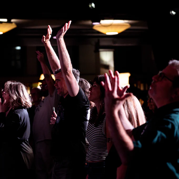 A group of people in the audience, with one person with their arms raised in the air.