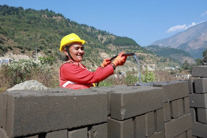 A woman pouring water in hardened bricks made of climate friendly locally awailable materials to construct CSEB model & stone masonry houses. 