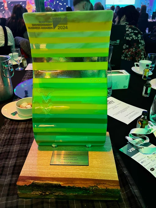 Edinburgh Remakery's Vibes Award tropy sitting on a table. The award is curvy glass with varying green horizontal stripes