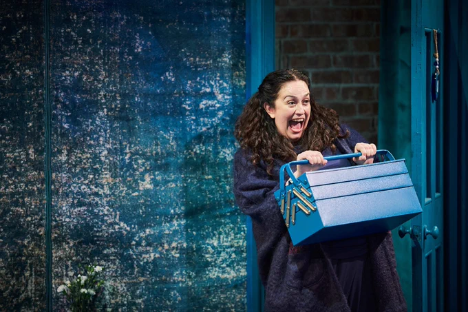 A woman smiles enthusiastically holding a box. Everything is blue.