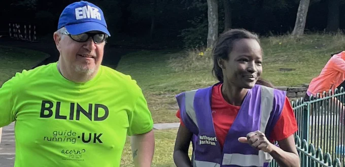 Southport parkrun regulars. Zana in red T-shirt guiding James who is  wearing his guide running his vis T-shirt, blue cap and cool shades