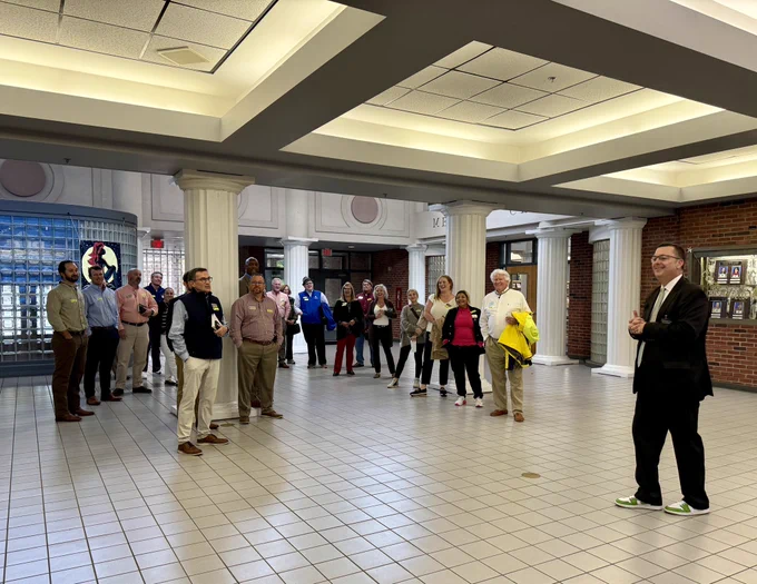 Group of people in school lobby listening to man in suit