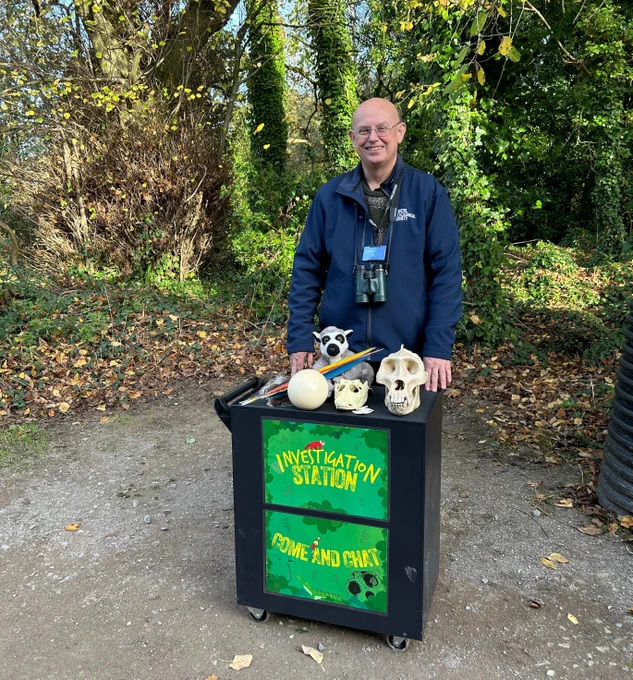 Person standing next to a cart labeled "Investigation Station, Come and Chat!" displaying various skulls.