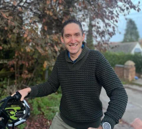 John, the new Transition Stroud e-bike coordinator, is standing holding a bike. Behind him is a tree... it looks like autumn.