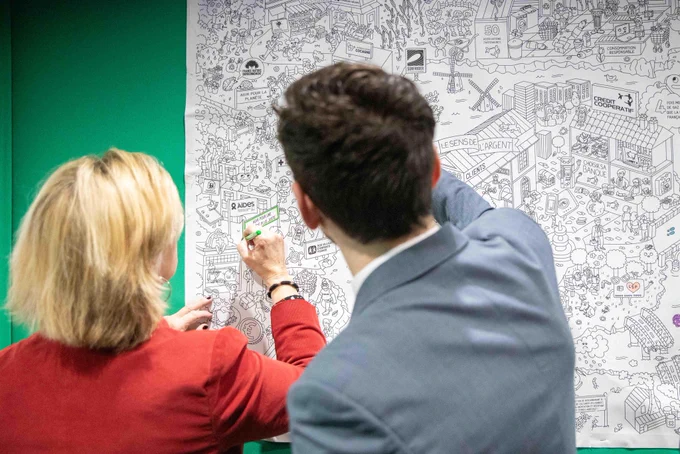 La ministre colorie une grande fresque posée sur un fond vert.