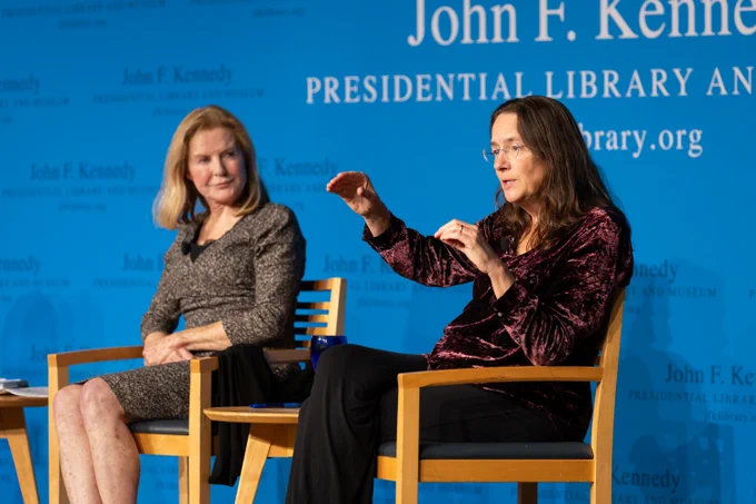 Heather Cox Richardson (right) and Margery Eagan (left) seated on stage at the John F. Kennedy Presidential Library and Museum, with Richardson in the foreground gesturing during a discussion.