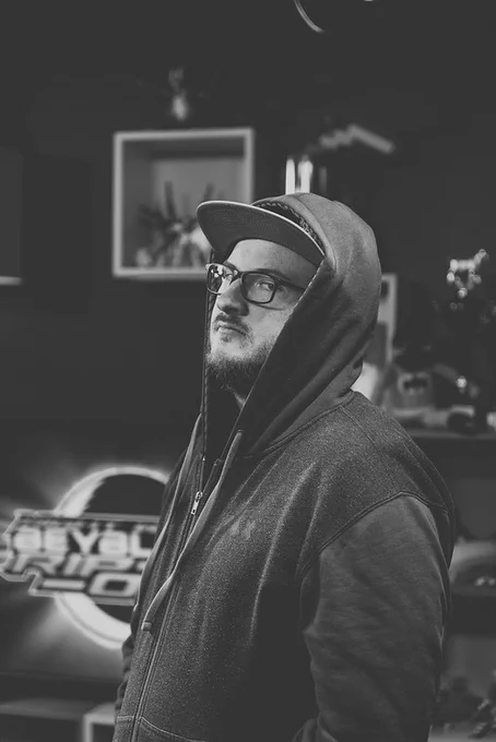 Black and white photo of Jordan Hopkins looking tough in a hoodie in front of the Night Watch Beyblade Rip-Off logo. 