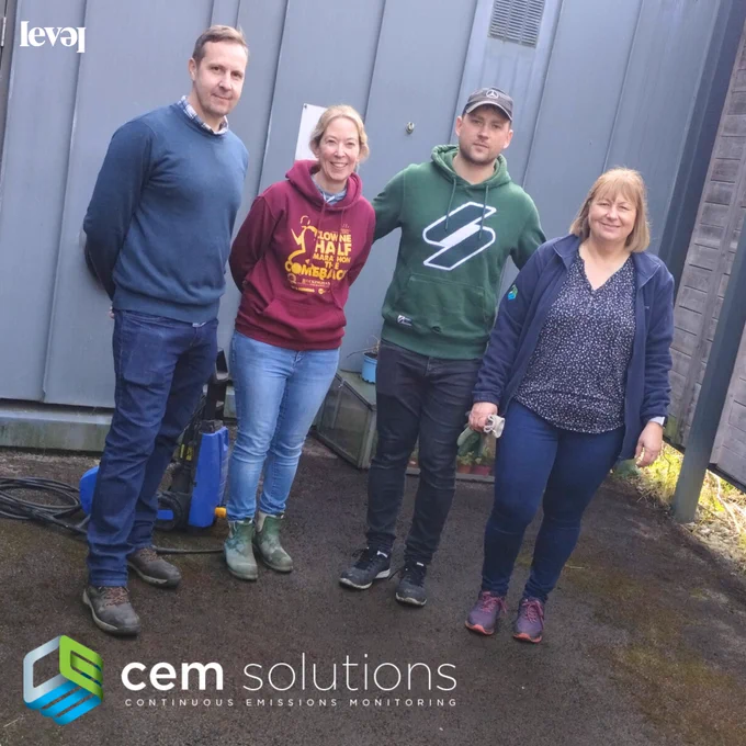 A group of four people stand together in an outside courtyard area. They smile at the camera. It looks like they've been doing some clearing and cleaning work as they have a blue pressure washer with them. Behind them is a grey zinc clad wall. The CEM Solutions logo in green, blue and white sits at the bottom of the screen.