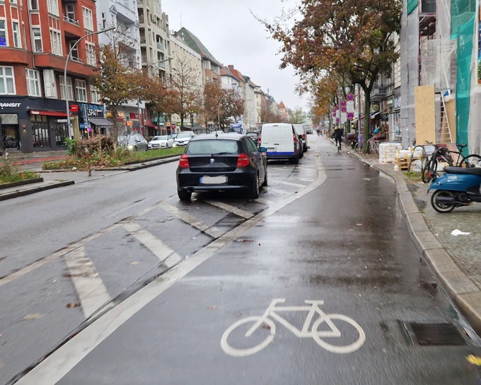 Fußgängerüberweg über Radweg (rechts) und einen Fahrstreifen (links) dazwischen eine markierte Sperrfläche mit einem darauf stehenden Kfz.