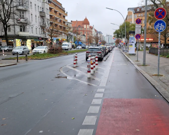 Fußgängerüberweg über Radweg (rechts) und einen Fahrstreifen (links) dazwischen eine markierte Sperrfläche geschützt mit 7 Pollern.
