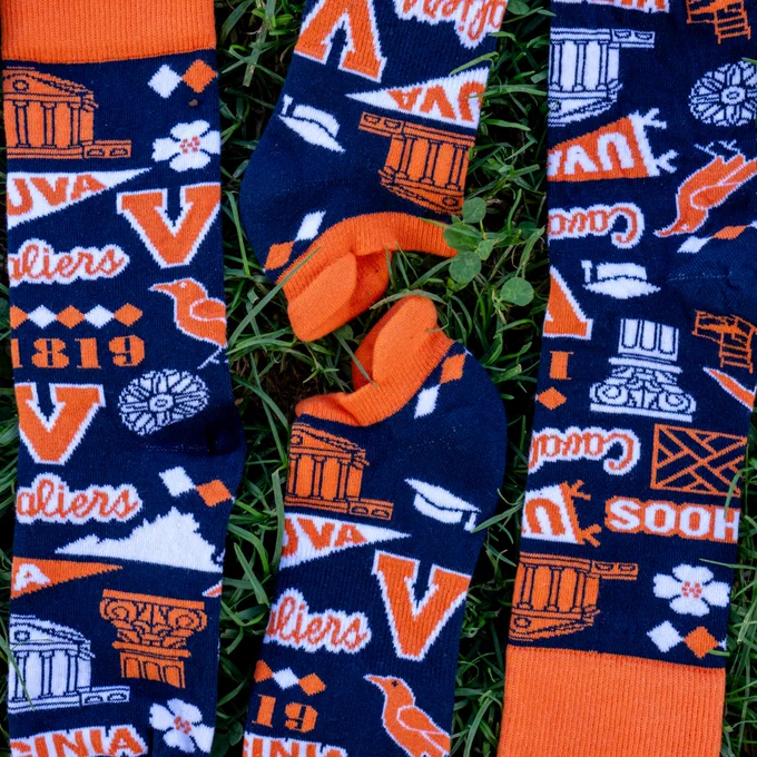 A collection of University of Virginia Cavaliers-themed socks in orange and blue, featuring various symbols and icons related to the university, displayed on a grassy background.