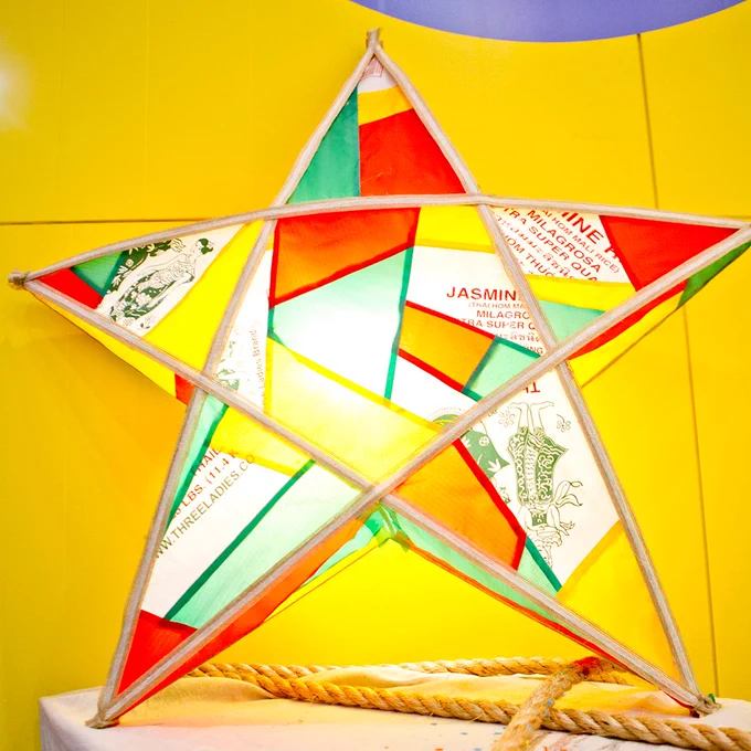 A colorful parol lantern displayed against a yellow background, featuring various prints and names in Tagalog.