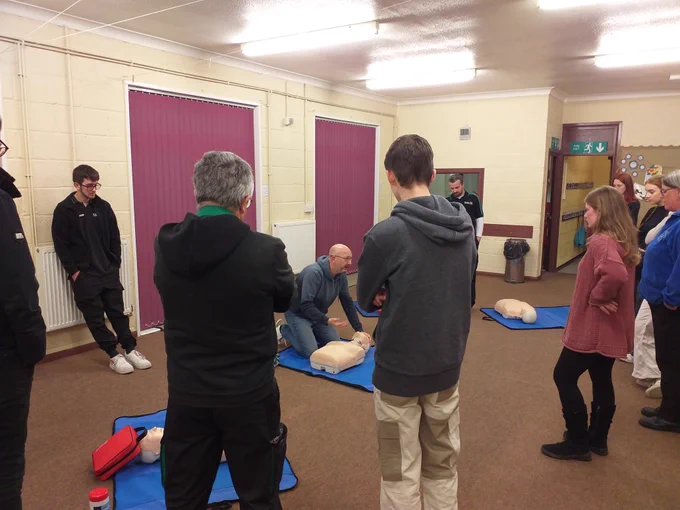 Members of the Community First Aid Network observing the Training Lead demonstrating Basic life Support