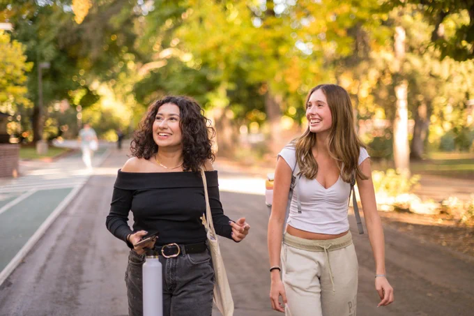 Two students look up while walking and smiling on Chico State campus.