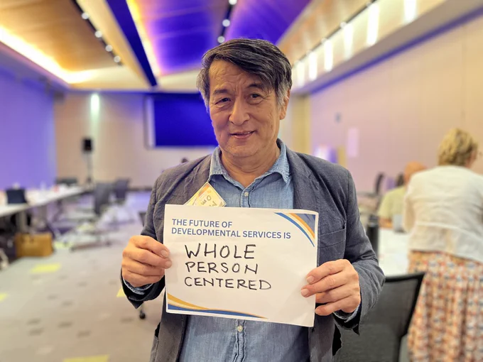 Image of a man holding a sign that says The Future of Developmental Services is Whole Person Centered.