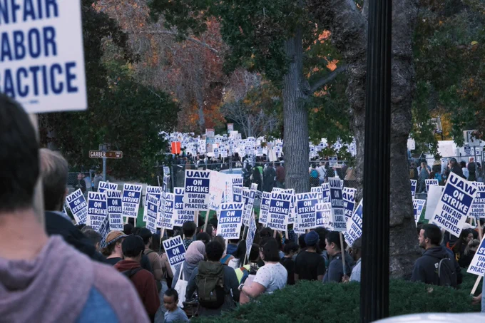 Large crowd of people holding strike picket signs and walking down a street