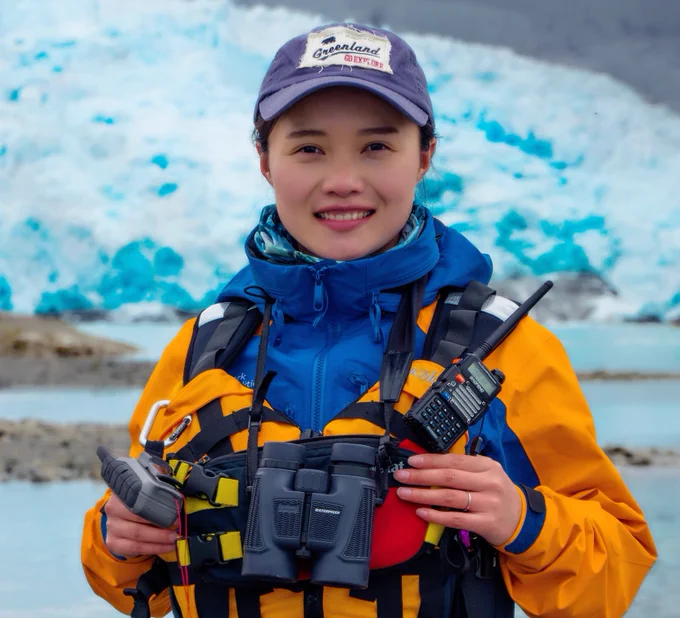 Dr Chen Zhao wearing a thick jacket and an orange vest standing on an ice sheet and smiling