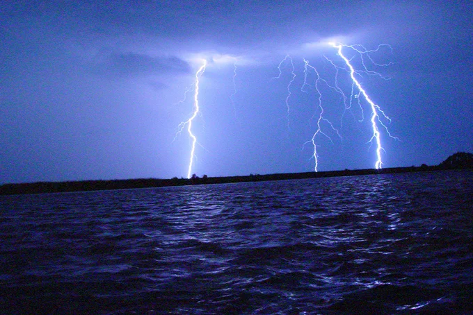 A nighttime scene over a large body of water showcasing multiple bright lightning strikes illuminating the sky.