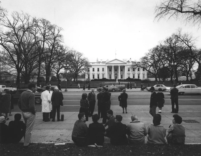 Groups of people stand on the street outside the White House on November 22, 1963.
