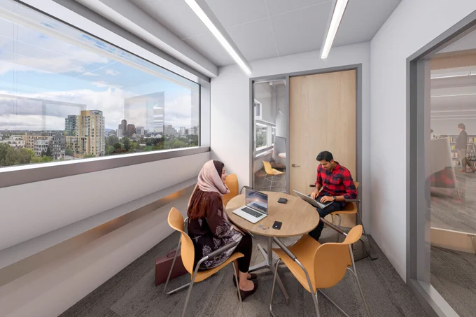 Two people seated at a round table in a room with windows.