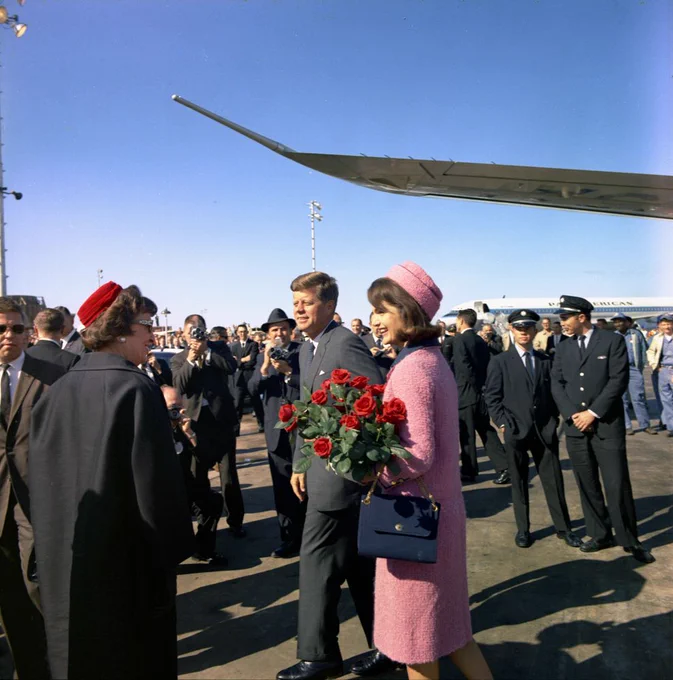 Mrs. Kennedy carries a bouquet of red roses and walks next to John F. Kennedy on the tarmac at Love Field in Dallas, Texas.