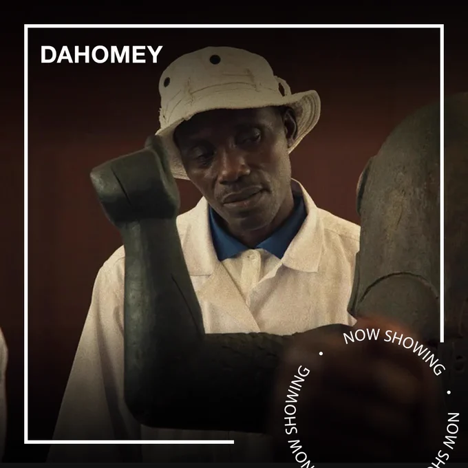 A man looks at an African sculpture. Text - Dahomey, Now Showing