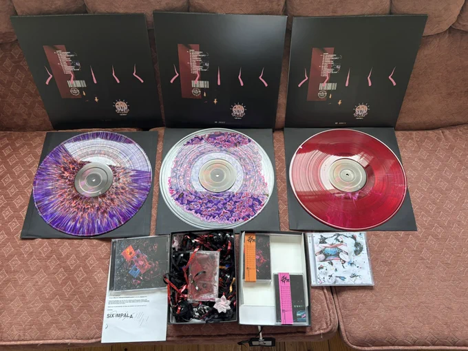 3 vinyl variations of RUBBER by six impala, 1 CD of RUBBER by six impala, 1 CD of WFLYTD by six impala, 1 cassette of RUBBER by six impala, 1 cassette of RUBBER ALT by six impala and the crushed cassette from the cover of RUBBER by six impala all displayed next to each other