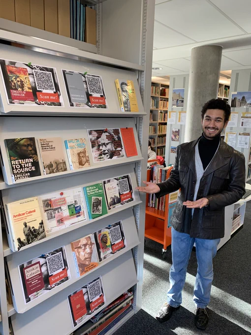 Neo, Cabral book display curator, posing with the display in the sunshine - come see it in the Library until 17th January 2025.