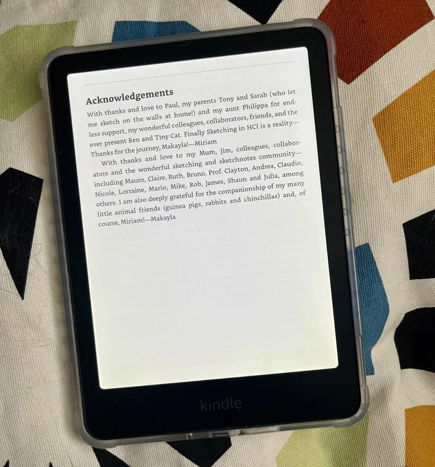 A Kindle device displaying the Acknowledgements page of the book Sketching in Human-Computer Interaction. The text includes expressions of gratitude from the authors, Makayla and Miriam, to their families, colleagues, collaborators, and members of the sketching and sketchnotes community. It also mentions appreciation for animal companions like cats, guinea pigs, rabbits, and chinchillas. The Kindle is resting on a patterned fabric background.