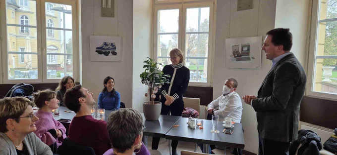 Eine Gruppe von Menschen (NaWik-Team) sitzt an einem Tisch in einem Restaurant und lacht. Beatrice Lugger steht vor einem kleinen Zitronenbäumchen, das auf dem Tisch steht.