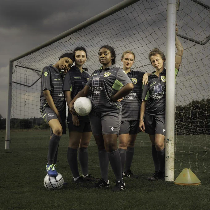 A female only football team stood on the pitch next to a goal post.