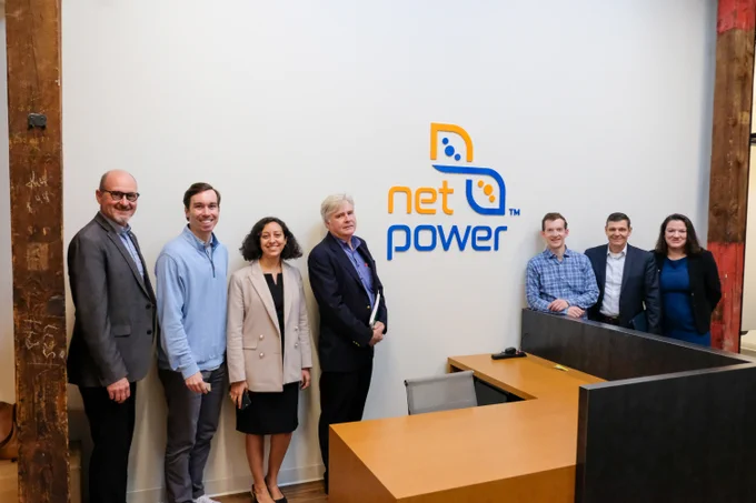 A group of seven people posing for a group photo in front of a white wall with the net power logo on

