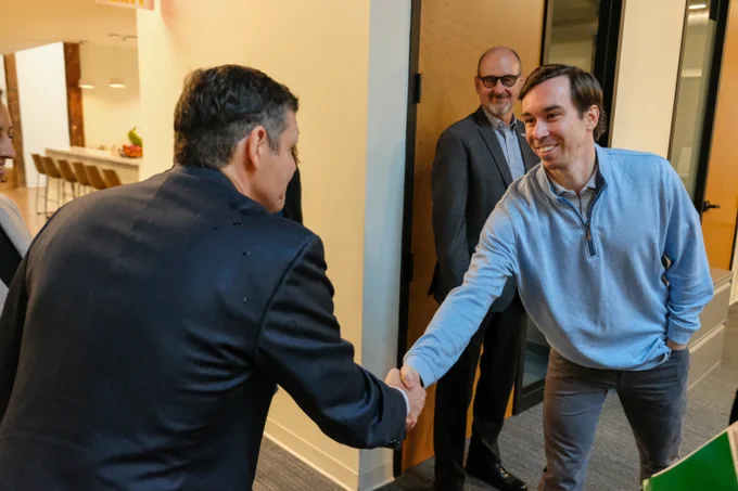 Two men shaking hands while a third looks on

