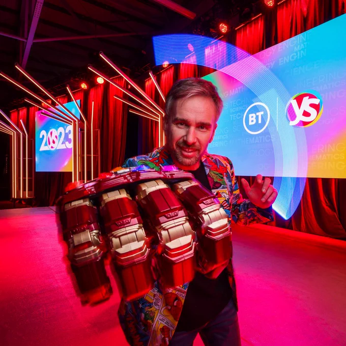 Photo of man on brightly lit multicoloured stage wearing a superhero hand