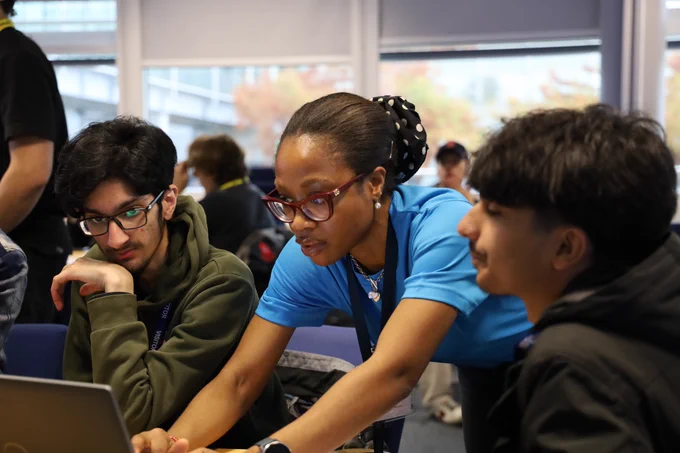 An Abbott Group volunteer helping two male students code on a laptop 