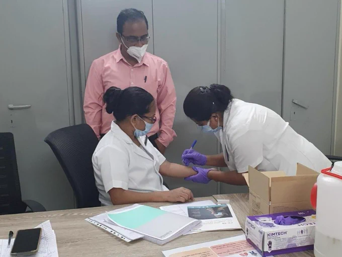 A woman giving a skin test to a healthcare worker while a man watches