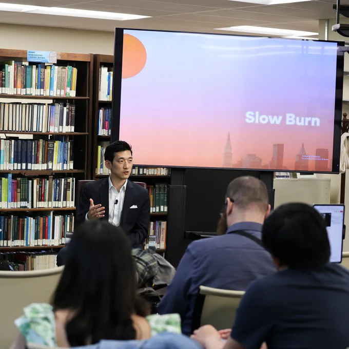 R. Jisung Park is seated, speaking to an audience, with bookshelves and a screen that says "Slow Burn" behind him.