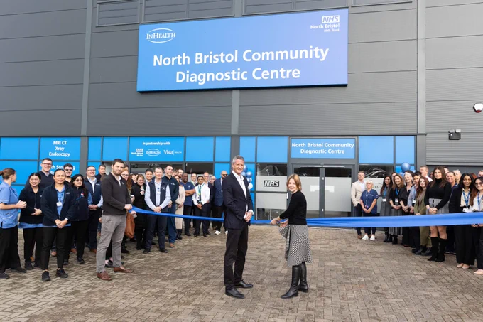 People gathered outside a building with a sign "North Bristol Community Diagnostic Centre". Two people stand cutting a blue ribbon.
