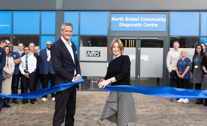 A building with a sign "North Bristol Community Diagnostic Centre". Two people stand cutting a blue ribbon.