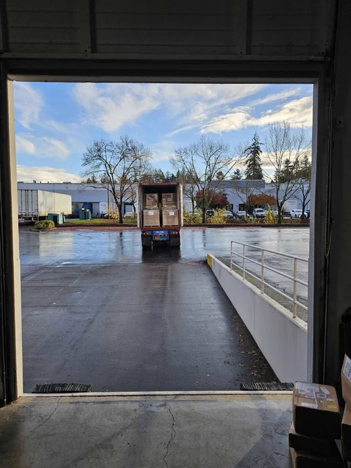 A truck full of boxes of Triangle Agency games sits at a distance away from a large, mostly empty shipping container where the photo is being taken from.