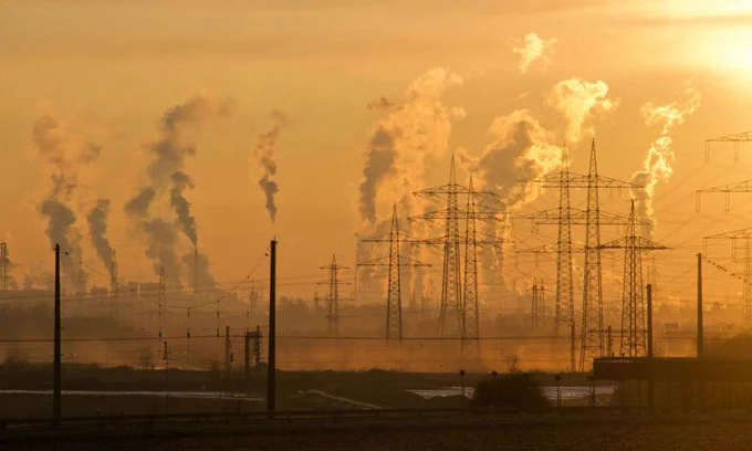 A hazy landscape affected by wildfire smoke, featuring obscured visibility and distant trees and buildings in the background. Phone and network poles are visible in the foreground, emphasizing the impact of air quality on the environment and urban infrastructure.
