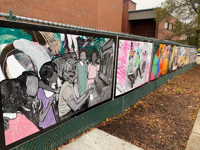 The entire fence mural, showing 8 panels of paintings from the aadl archives receding into the distance, with the brick of the downtown library behind.