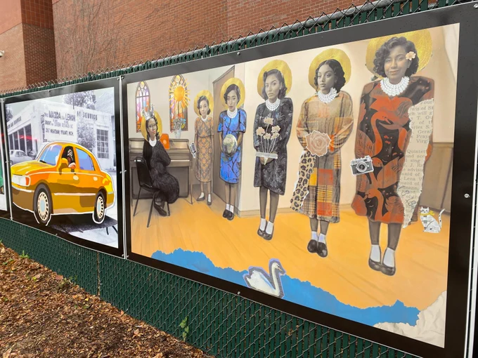 An angled perspective of two panels on a green fence with the brick of the Downtown Library in the background. The panel on the left shows a bright yellow car superimposed over a black and white photo of a driver with a sign mounted on top of the car saying "This MAZDA is a LEMON". The closer photo shows 6 Black women in collage, with one seated at a piano, each wearing dresses, white socks, and black shoes, with golden haloes around their heads. Stained glass windows in the background and a swan swimming in blue water in the foreground