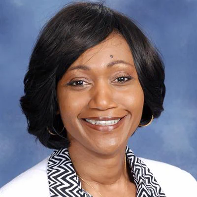 Portrait of an individual with a warm smile, short black hair, wearing a black and white patterned top.