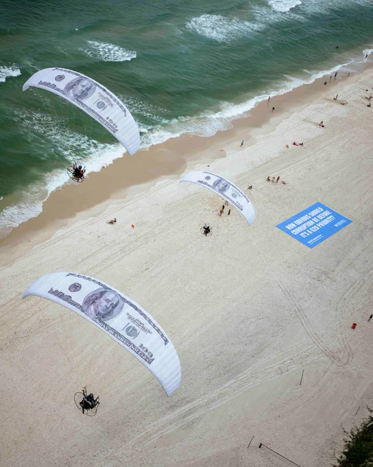 Paragliders with canopies customised with US$100-bill designs flying in over a beach Rio