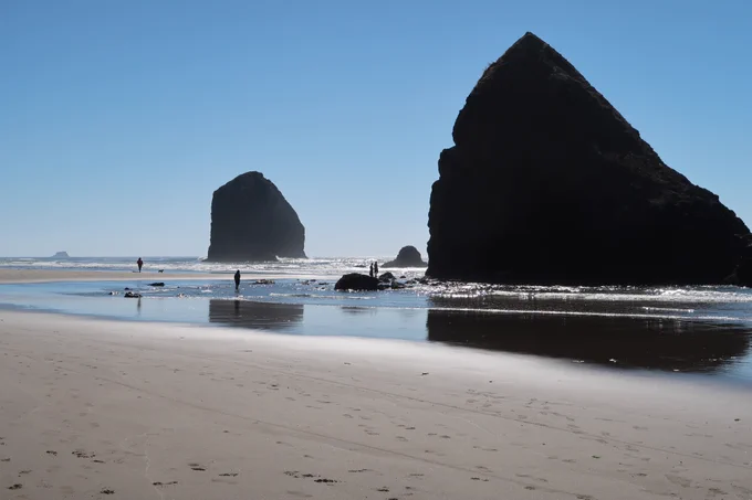 Blue skies at Cannon Beach Oregon with Haystack Rock and people wading the water. Land of puffins if you go at the right time. 